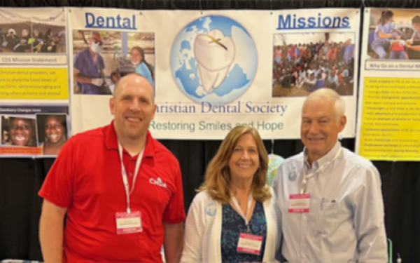 Three people standing in front of a Christian Dental Society booth with banners about dental missions.